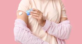 Woman wearing pink shirt applying a glucose monitor to her arm.