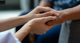 A pair of hands gently hold a second pair of hands in a manner of care and support.