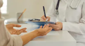 a patient sitting down with a medical professional taking notes on a clipboard. 