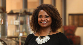 A headshot of Dr. Jamie Barner. Dr. Barner is smiling to camera, wearing a black shirt and gold and white statement necklace.