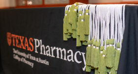 A close-up of green and white academic cords on a Texas Pharmacy-branded table.