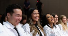 Three pharmacy students in white coats smiling.