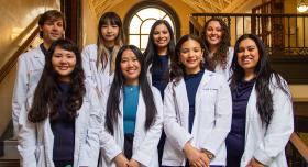 Eight students in white coats smiling.