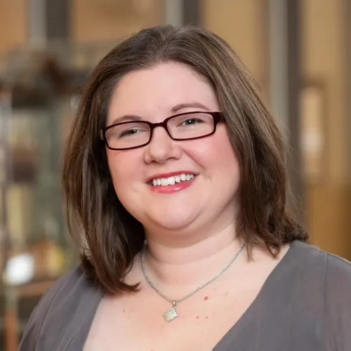 Jessica Bloodgood wearing a necklace and glasses and smiling.