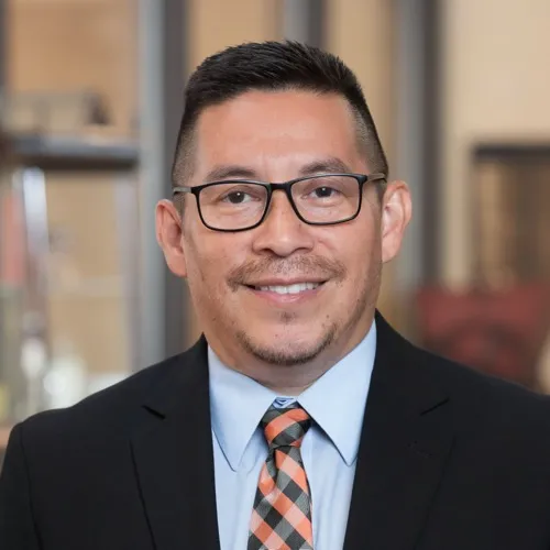 Greg Caldera wearing a suit, checkered tie and glasses.