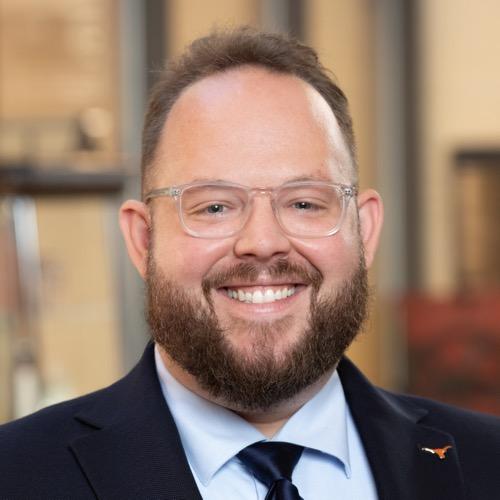 Dr. Travis Carlson wearing a suit and tie and glasses.