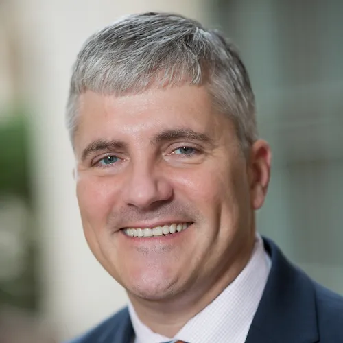 Dean Poloyac wearing a suit and smiling.