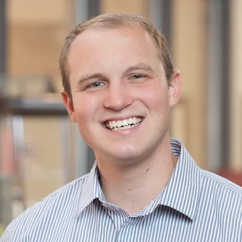 Chris Roscoe wearing a striped collared shirt and smiling.