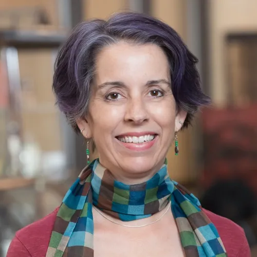 Rebecca Schwarz wearing earrings and a checkered scarf and smiling.