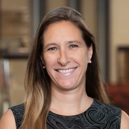 Nicole Toomey wearing earrings and a sleeveless top and smiling.