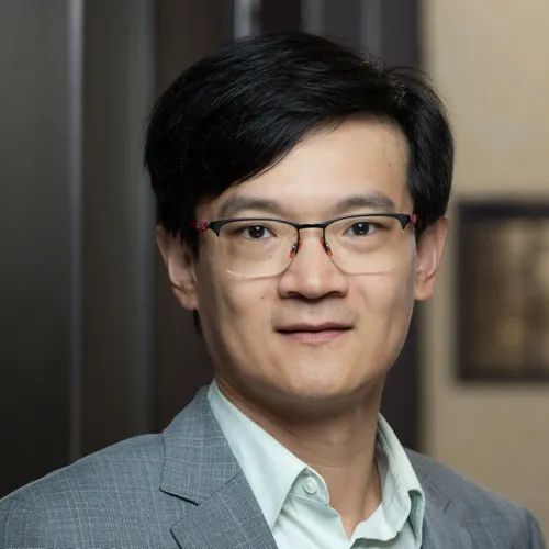 A man wearing glasses with a suit coat and collared shirt.