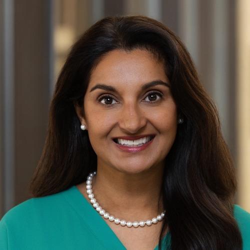 A woman wearing pearls and smiling.