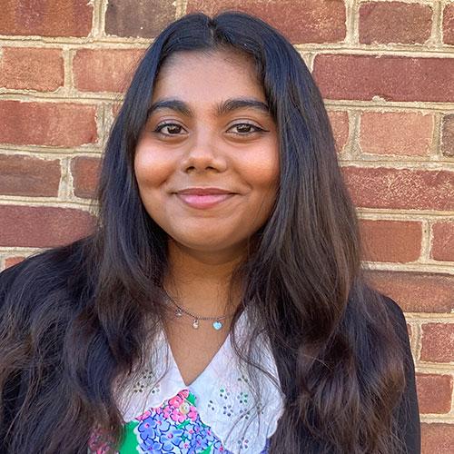 Damini Nair smiling and standing in front of a brick wall