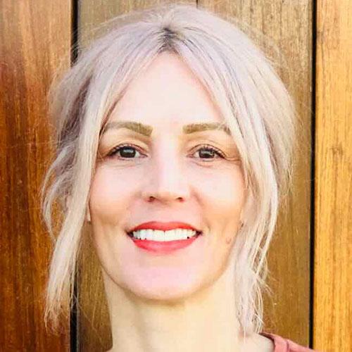 Sara Young smiling and standing in front of a wooden wall.