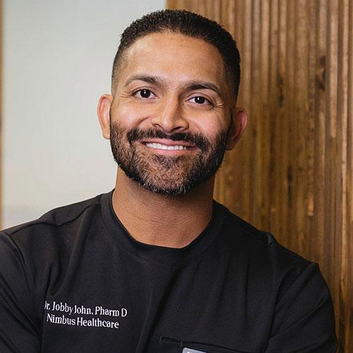 Dr. Jobby John smiling and wearing black scrubs