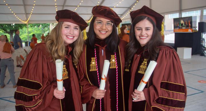 Three women in regalia holding diploma scrolls.