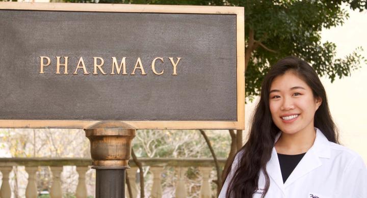 A woman smiling next to a sign that says "Pharmacy."