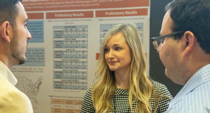 Three people having a discussion in front of a research poster.