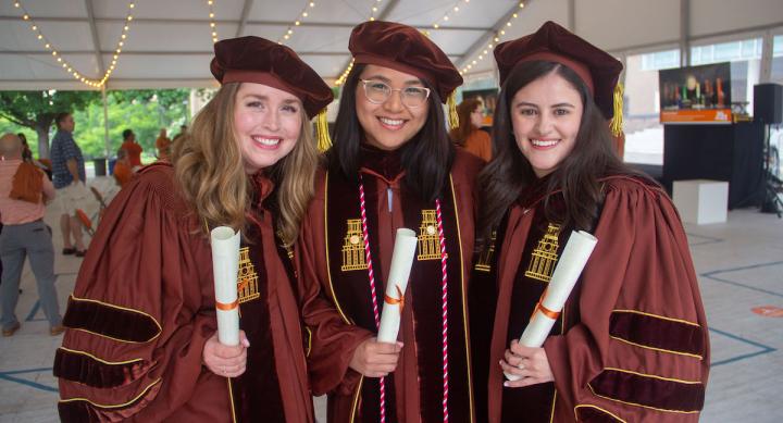 Three woman in doctorate regalia holding diplomas.