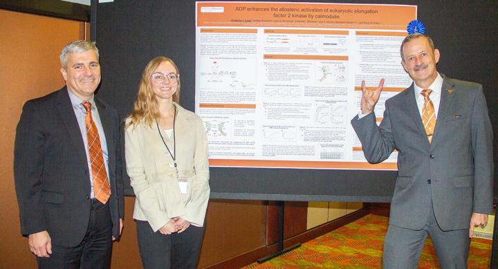 Three people standing in front of a research poster. One person is giving the Hook 'em Horns hand gesture.