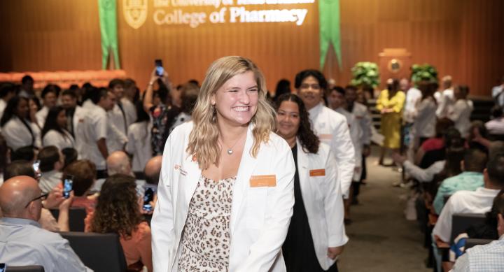 A blonde student wearing a white coat walking in the processional at the White Coat ceremony