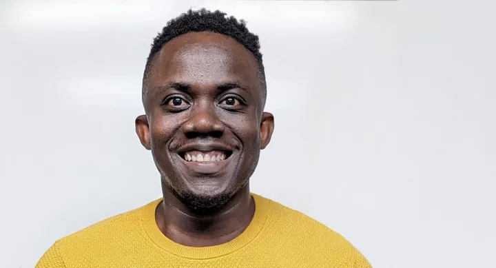 A man smiling and wearing a light sweater.