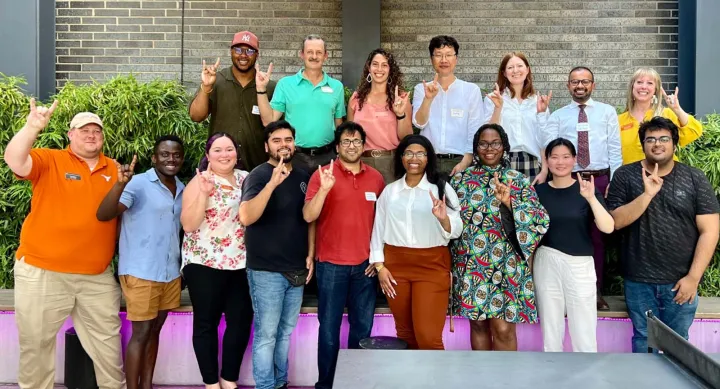 A group of people smiling and giving the Hook 'em Horns hand gesture.