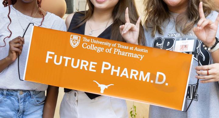 Three people giving the Hook 'em Horns hand gesture and holding a "Future Pharm.D." banner.