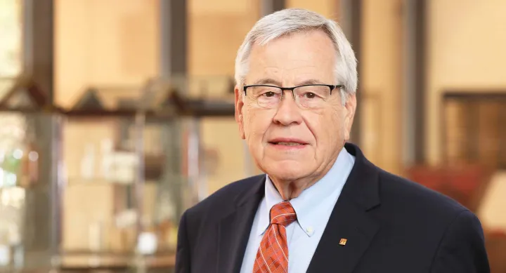 A man wearing a suit, tie and glasses and smiling.