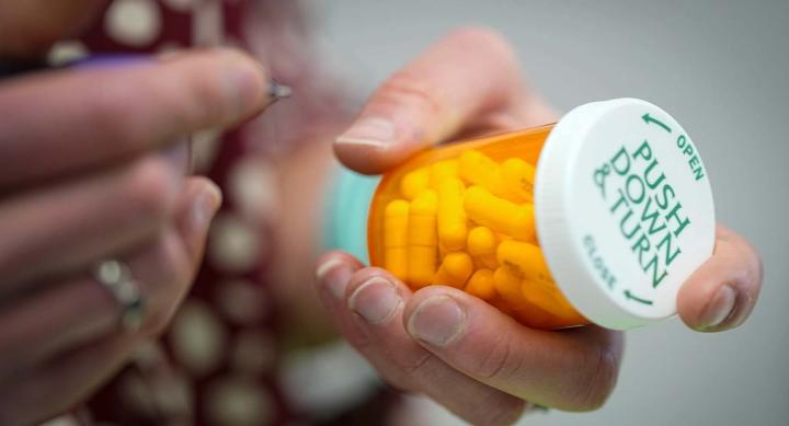 Two hands, one of them holding a prescription medication bottle full of capsules..