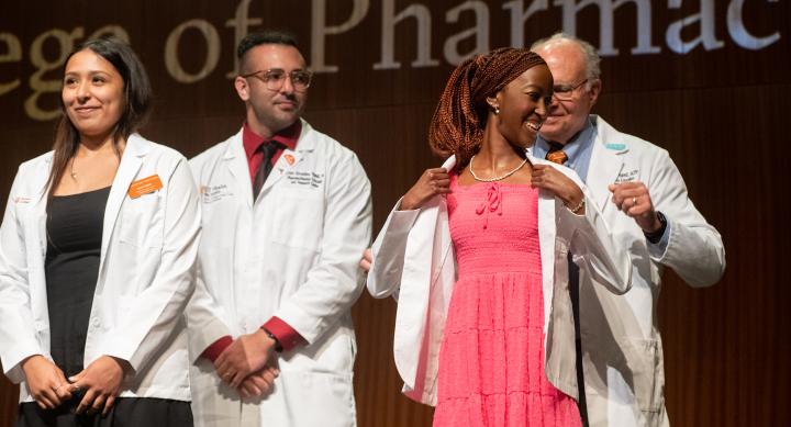 Two new pharmacy students receiving white coats from faculty at the White Coat Ceremony