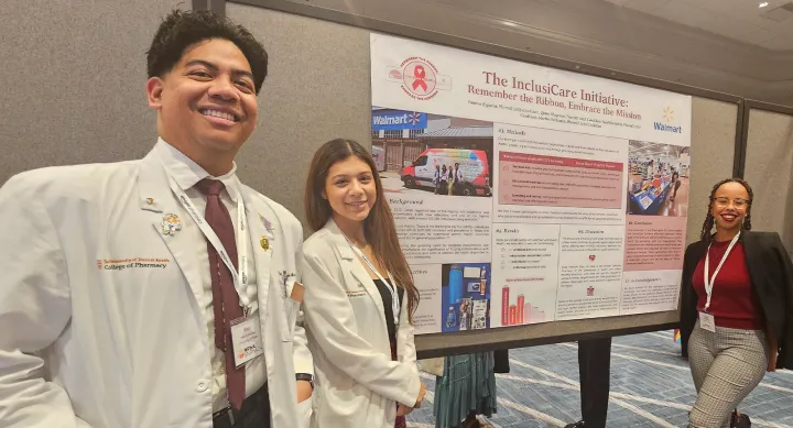A group of Pharmacy Students smiling in front of a poster presentation set up.