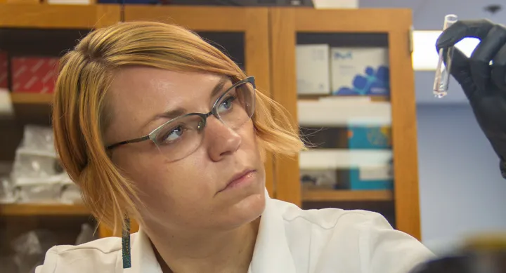 Someone in a lab white coat looking at a small test tube.