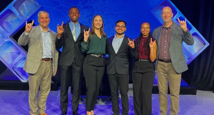 Six people smiling and giving the Hook 'em Horns hand gesture.