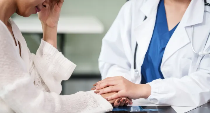 Stock image of a female physician holding the hand and comforting a female patient.