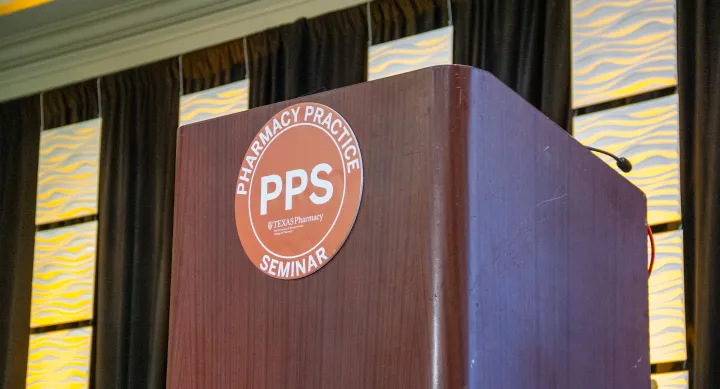 A dark wooden podium with an orange circle logo that reads "Pharmacy Practice Seminar" around the edge and "PPS" in the center. 