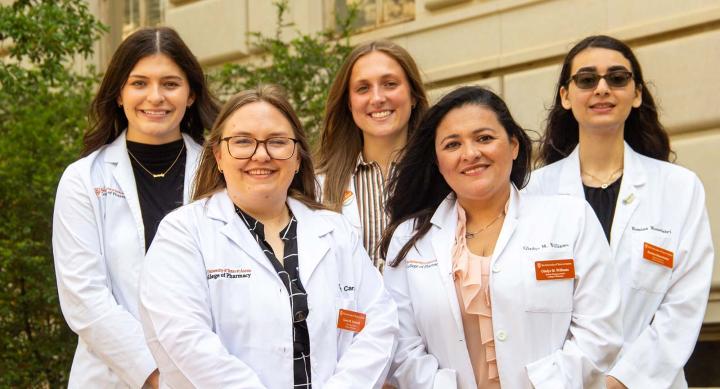 Five women wearing white coats and smiling.