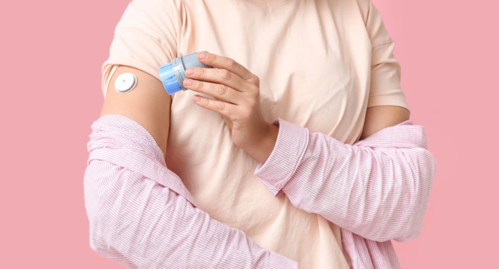 Woman wearing pink shirt applying a glucose monitor to her arm.