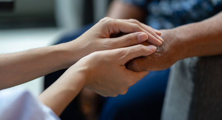 A pair of hands gently hold a second pair of hands in a manner of care and support.