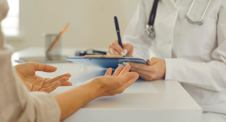 a patient sitting down with a medical professional taking notes on a clipboard. 