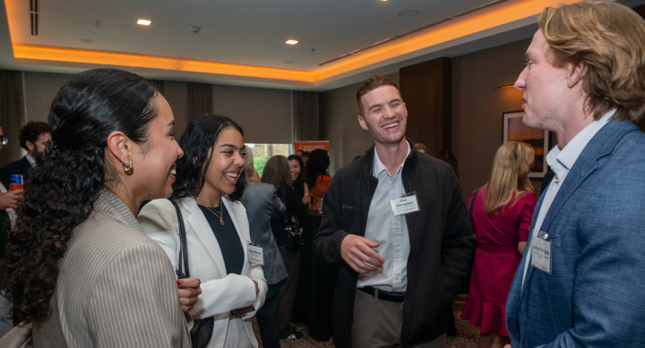 Three young professionals laugh and talk at a networking event. All are dressed in business casual attire.