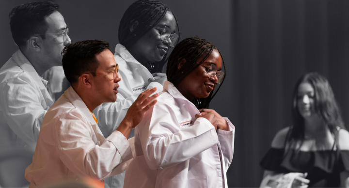 On stage at a white coat ceremony, a pharmacy student puts on her first white coat with the help of a faculty member.