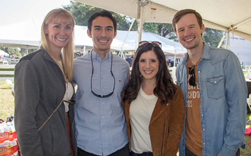 Four alumni smiling and standing in the homecoming tailgate tent